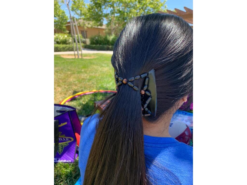 Woman outdoors wearing a black African Butterfly Ndebele Thick Hair Comb in a low ponytail hairstyle adorned with black and brown beads