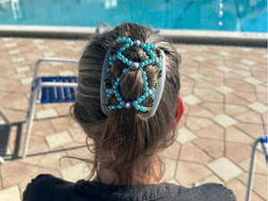 Woman with silvery gray hair sitting poolside wearing a gray African Butterfly Ndalena Hair Comb with gray, blue, black and gold beads in a French twist hairstyle