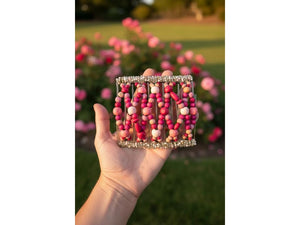 Woman holding an African Butterfly Wire Hair Clip 11 Tong 526 in a rose garden, pink and magenta beads, warm sunlight